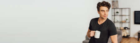 Panoramic shot of handsome man holding cup of coffee at homeの写真素材