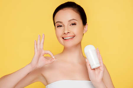 smiling woman holding stick deodorant and showing ok sign isolated on yellowの写真素材