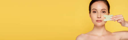 beautiful naked woman facial jade gua sha isolated on yellow, panoramic shotの写真素材