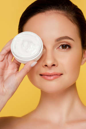 portrait of beautiful naked woman holding container with cosmetic cream isolated on yellowの写真素材