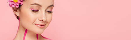 smiling beautiful woman with pink lines on body and flower isolated on pink, panoramic shotの写真素材