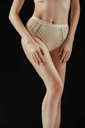 Cropped view of woman in beige panties touching leg isolated on black