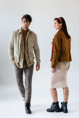 full length view of trendy couple posing on gray while man looking at camera on gray