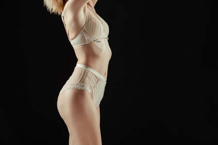 Cropped view of young woman in beige panties and bra isolated on blackの写真素材
