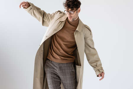 young man in trendy autumn outfit balancing isolated on gray