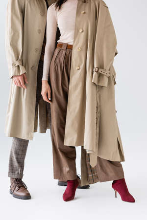 cropped view of fashionable couple in trench coats and trousers posing on grayの写真素材