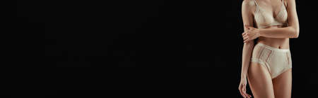 Horizontal image of woman in underwear touching arm isolated on blackの写真素材