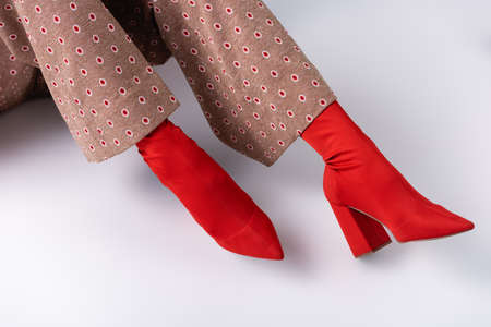 cropped view of woman in fashionable trousers and red boots sitting on white floor