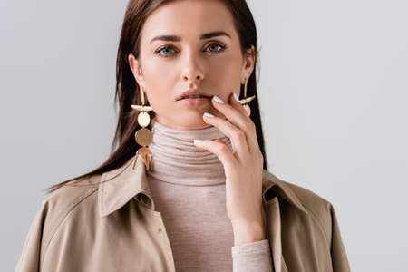 beautiflul, stylish girl touching face while looking at camera isolated on grayの写真素材