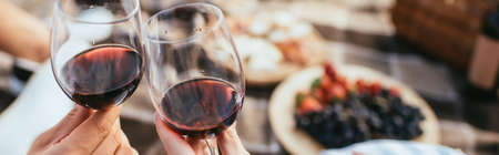panoramic crop of couple clinking glasses with red wineの写真素材