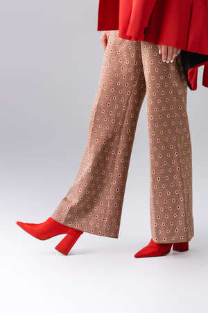cropped view of trendy girl in beige trousers and red boots on gray