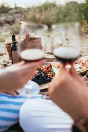 selective focus of plate with fresh fruits near bottle and couple clinking glasses with red wineの写真素材