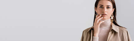 horizontal image of beautiful, elegant girl touching face while looking at camera isolated on grayの写真素材