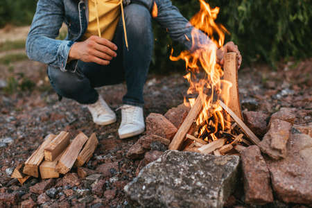cropped view of man sitting and putting log in burning bonfire
