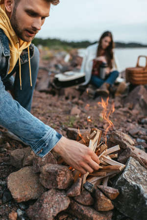 selective focus of handsome man touching sticks while making bonfire near womanの写真素材