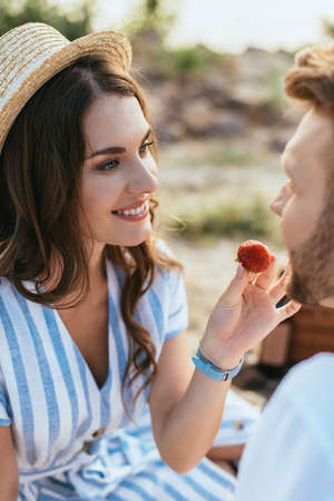 selective focus of happy woman in straw hat feeding boyfriend with strawberryの写真素材
