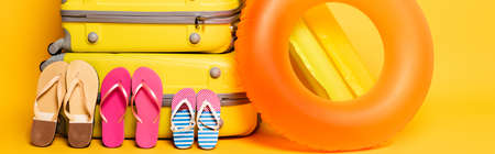 travel bags with family flip flops and pool floats on yellow, panoramic shotの写真素材