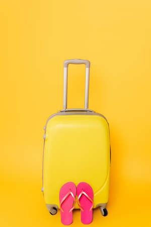 travel bag with pink flip flops isolated on yellow backgroundの写真素材