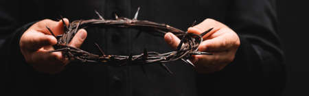horizontal crop of priest holding wreath with spikes isolated on blackの写真素材