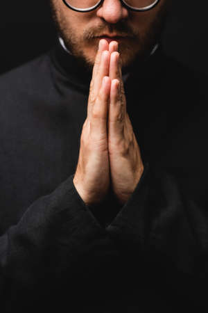 partial view of bearded priest with praying hands isolated on blackの写真素材