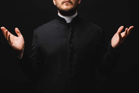 cropped view of priest with outstretched hands isolated on blackの写真素材