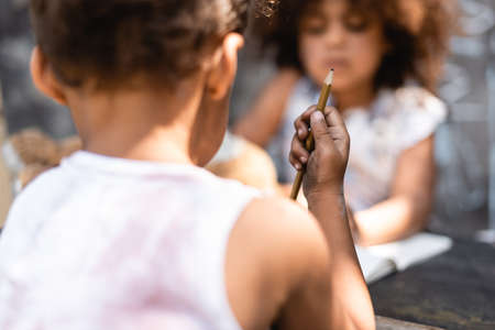 selective focus of poor african american kid holding pencil near sister