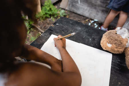 partial view of african american kid holding pencil while writing near childの写真素材
