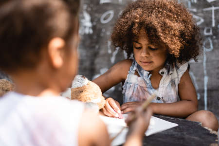 selective focus of curly and poor african american child writing near brother