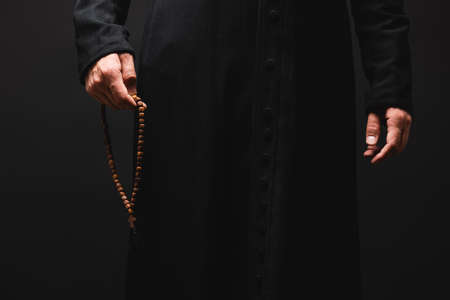 partial view of priest holding rosary beads in hand isolated on blackの写真素材
