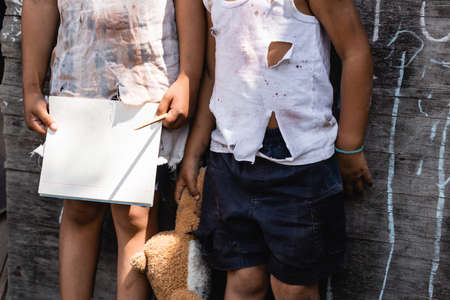 cropped view of poor african american kid in torn clothes standing with sister holding blank...