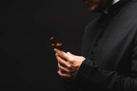 cropped view of priest holding cross isolated on black