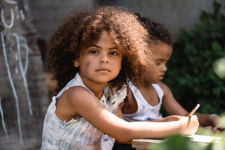 selective focus of african american kid holding pencil near brother sitting outsideの写真素材