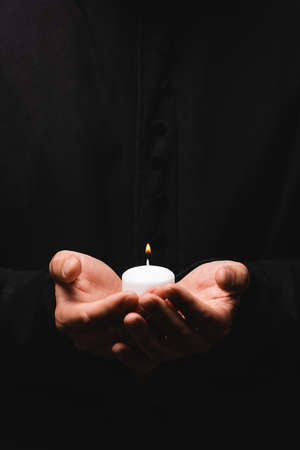 cropped view of pastor holding burning candle isolated on blackの写真素材