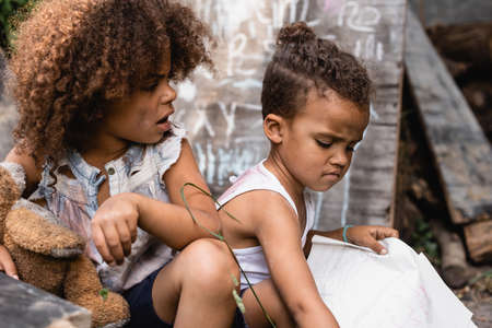 selective focus of poor african american kid with open mouth looking at brother holding paperの写真素材