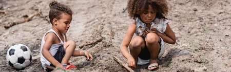 Panoramic crop of poor african american children playing on dirty road near football in slumの写真素材