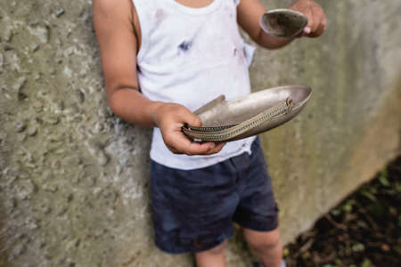 Cropped view of poor african american kid holding dirty spoon and plate on urban streetの写真素材