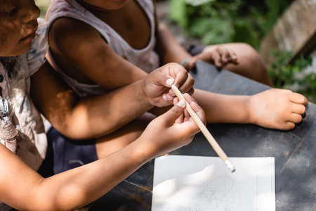 cropped view of poor african american kid holding pencil near notebook on desk and childの写真素材