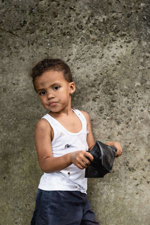 Beggar african american boy holding wallet near concrete wall on urban streetの写真素材