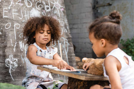 selective focus of poor african american kid writing in notebook near brother outside