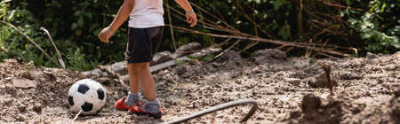 Panoramic crop of poor african american boy standing near football on dirty road on urban streetの写真素材