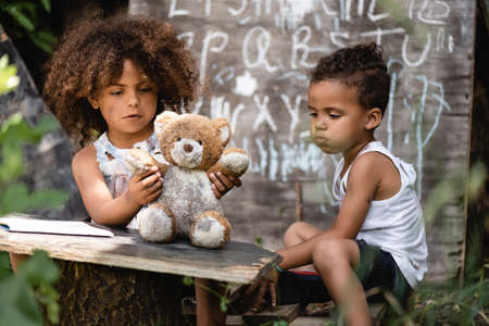 selective focus of poor african american kid playing with dirty teddy bear near brotherの写真素材