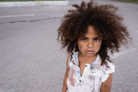 Poor african american child with messy face looking at camera on urban streetの写真素材
