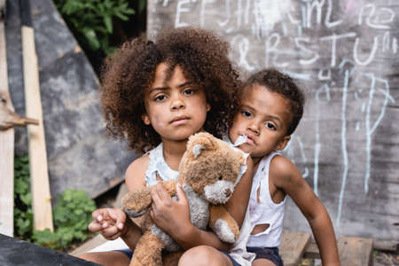 poor african american kids with dirty teddy bear looking at cameraの写真素材