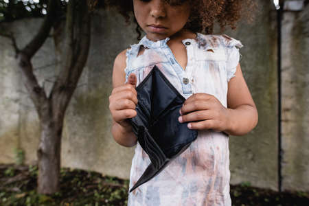 Cropped view of poor african american child holding empty wallet on urban street