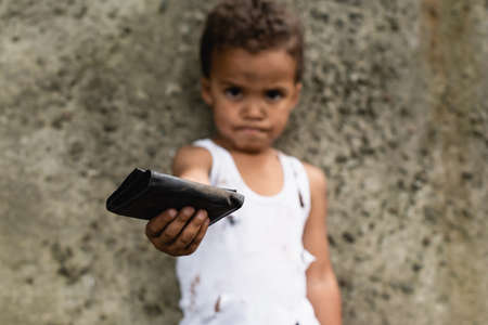 Selective focus of poor african american kid holding wallet on urban street