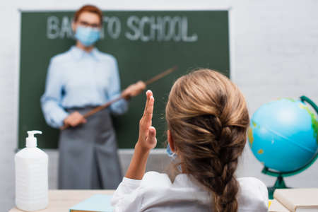 back view of schoolgirl with raised hand, and teacher with pointing stick near chalkboardの写真素材
