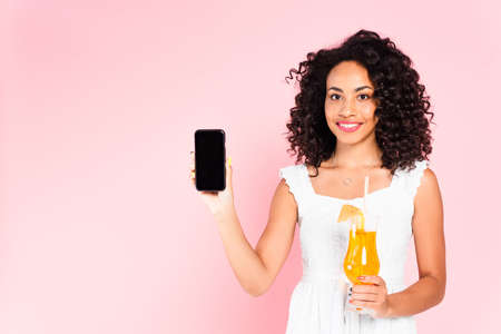 cheerful african american girl holding smartphone with blank screen and cocktail on pink