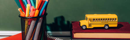 horizontal image of school bus model on books near pen holder with stationery on notebook near green chalkboardの写真素材