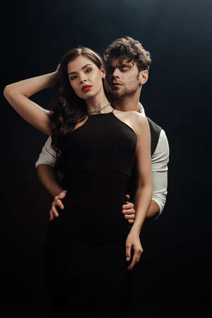 Handsome man embracing sexy woman with red lips on black background