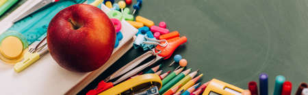 selective focus of delicious apple on book and school stationery on green chalkboard, panoramic conceptの写真素材